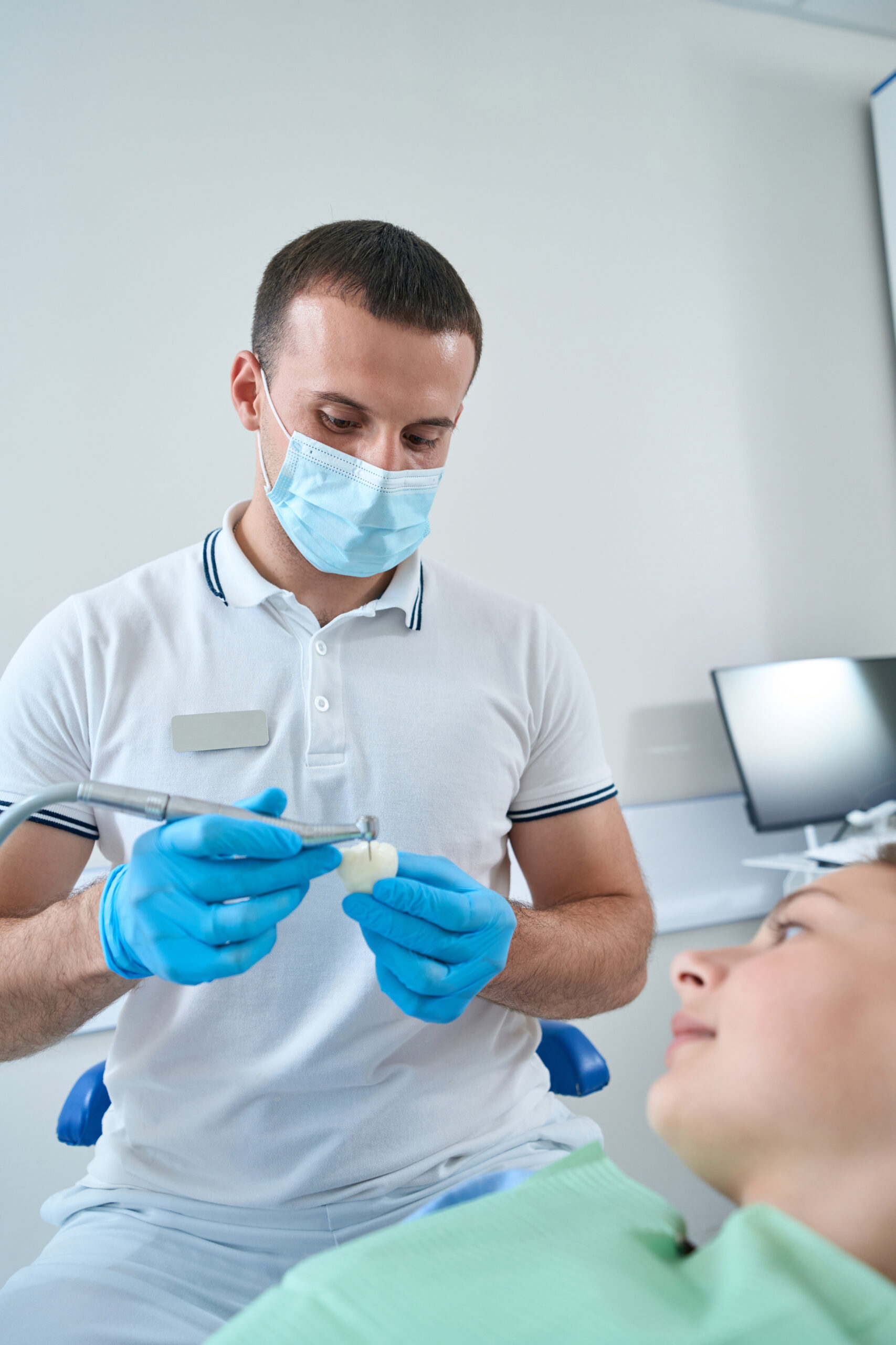 Experienced male doctor adjusting ceramic crown for young patient applying dental drill