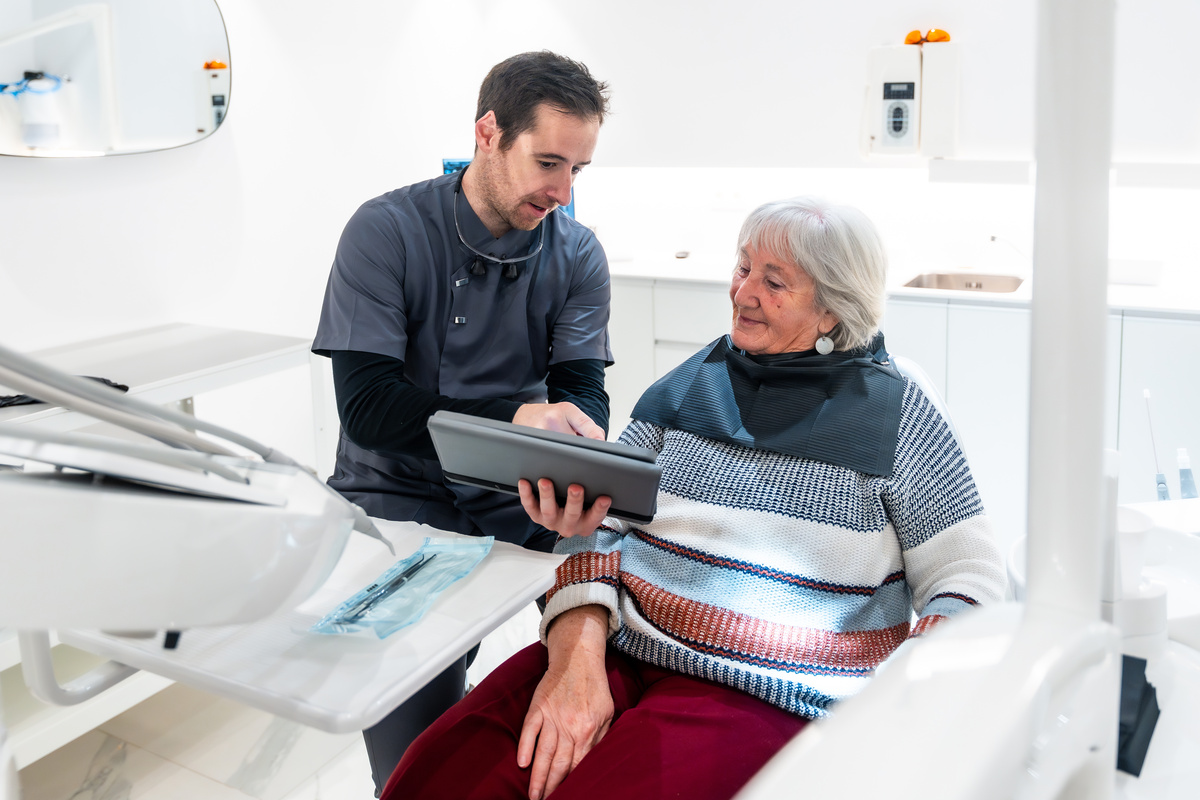 Dentist showing results on tablet to senior patient in dental clinic