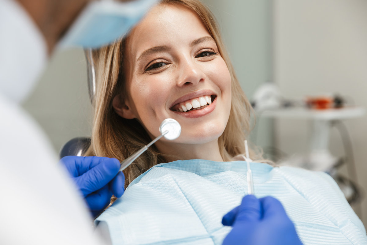 Image of satisfied young woman sitting in dental chair at medical center while professional doctor fixing her teeth